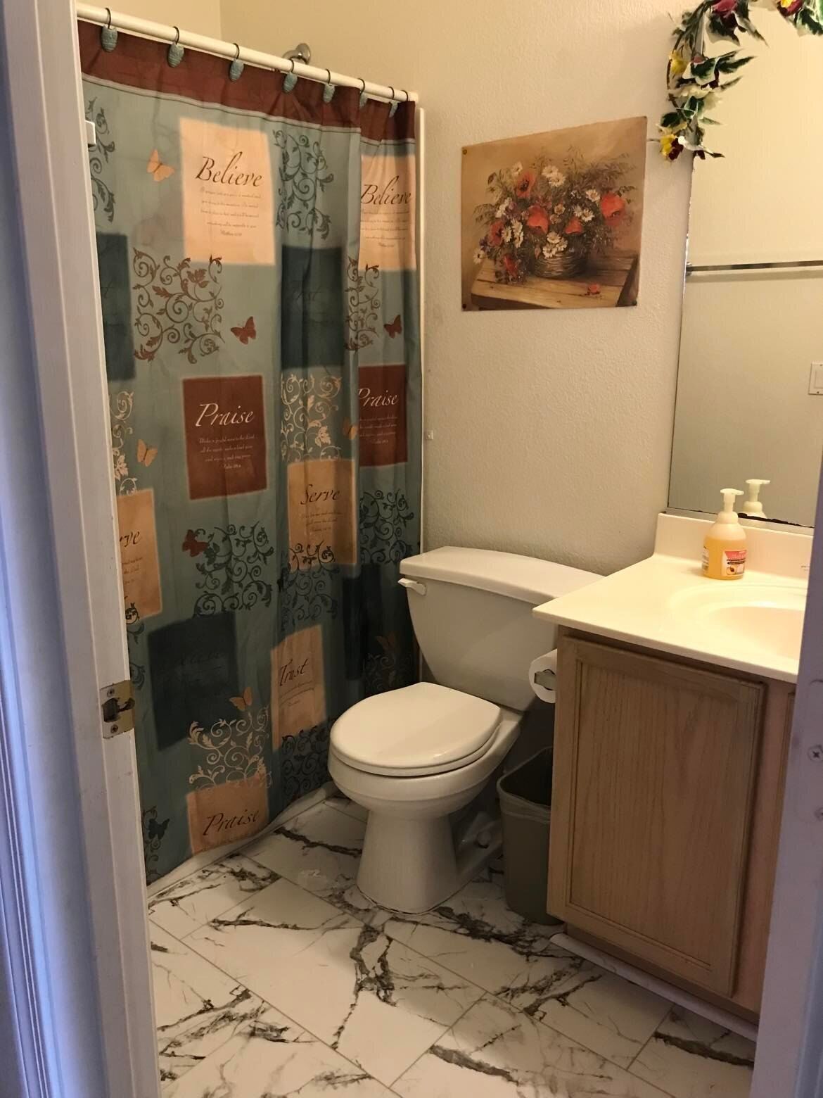 A bathroom with a toilet, a sink, and a shower curtain with motivational phrases.
