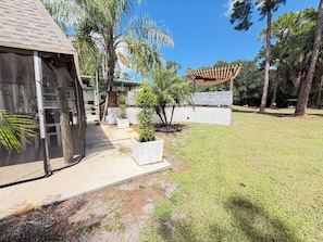 A residential property with a covered patio, a fenced yard, and a variety of trees.