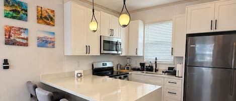 A modern kitchen with a central island, bar stools, stainless steel appliances, and pendant lighting.