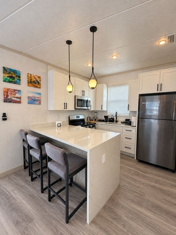A modern kitchen with a central island, bar stools, stainless steel appliances, and pendant lighting.