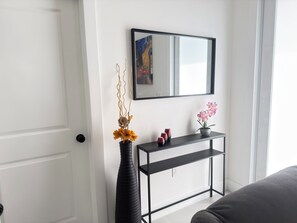 A minimalist room with a white door, a black console table with a mirror, and a vase with flowers.