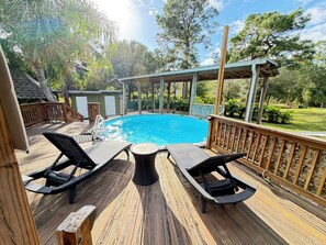 A wooden deck with a pool, lounge chairs, and a covered area.