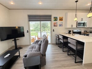 A modern living room with a sofa, TV, and a dining area with bar stools.
