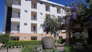 A multi-story building with balconies, a landscaped garden with a water feature, and a variety of plants. - Kirimathani Hotel (Mueang Loei)