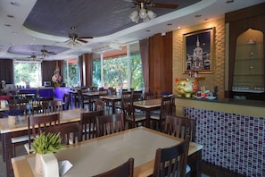 Ein Restaurant mit mehreren Tischen und Stühlen, Deckenventilatoren und einem großen gerahmten Bild an der Wand.