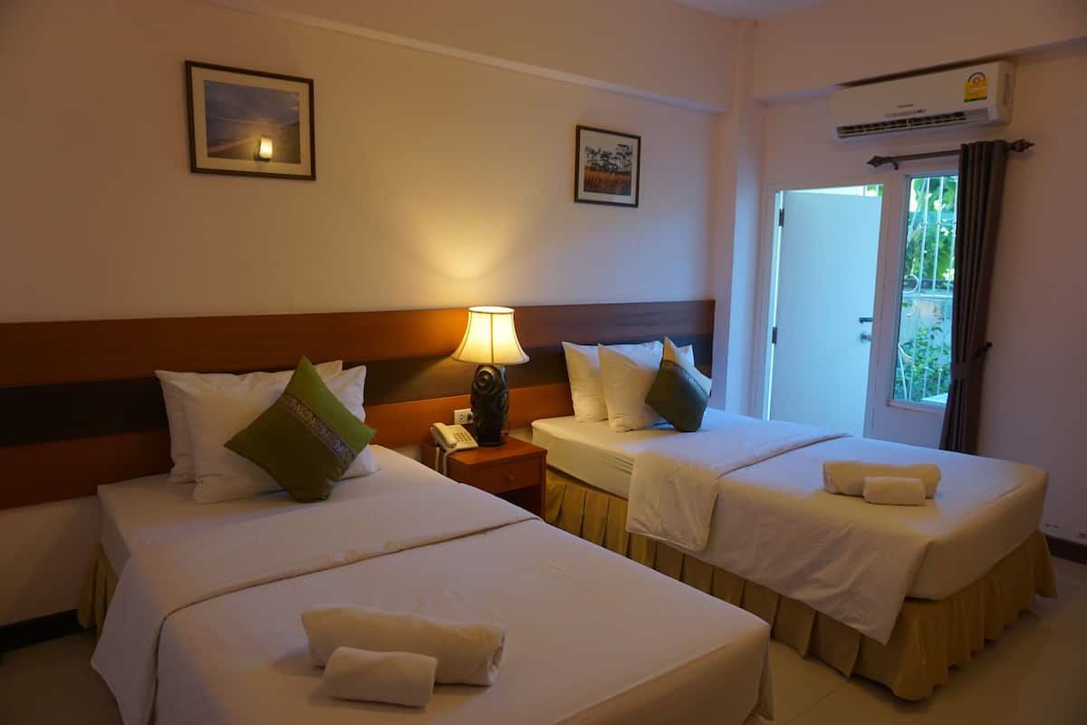 Una habitación de hotel con dos camas, una mesita de noche con lámpara y un equipo de aire acondicionado.