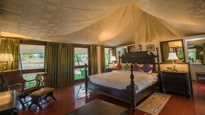 A spacious bedroom with a large bed, a chair, a desk, and a view of the outdoors. - Tuli Veer Bagh Resort (Ramtek)