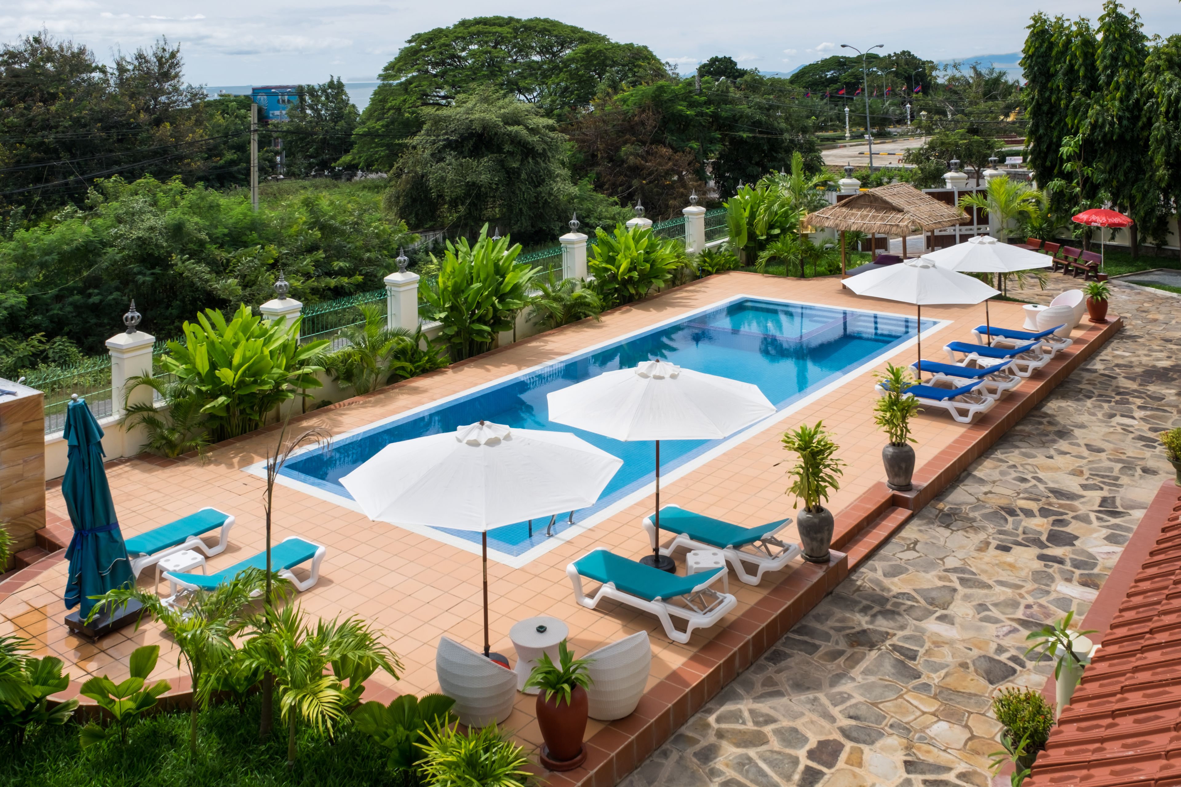A swimming pool with lounge chairs and umbrellas, surrounded by greenery and a stone pathway.