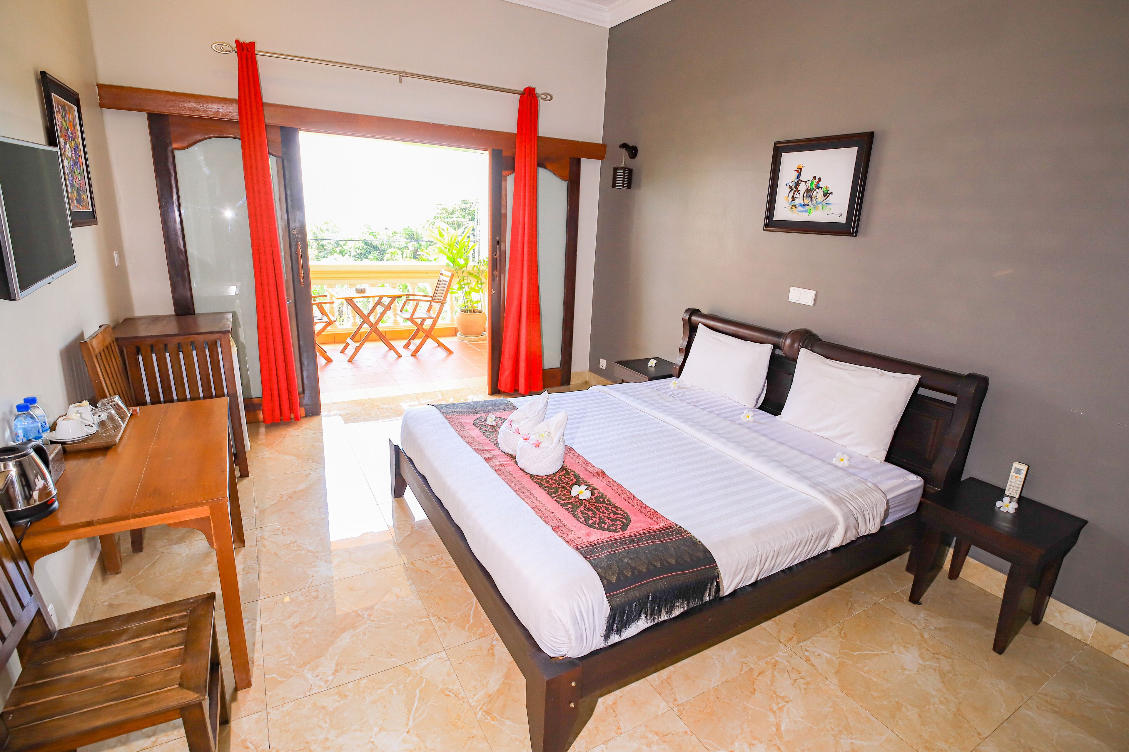 A hotel room with a bed, a desk, and a chair. There is a balcony with a table and chairs.