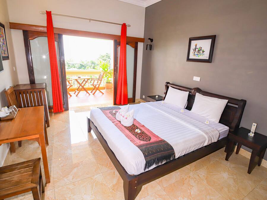 A hotel room with a bed, a desk, and a chair. There is a balcony with a table and chairs.
