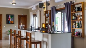 A bar area with a long counter, wooden chairs, and shelves with bottles. - Riviera Hotel & Resort Kep (Kep)