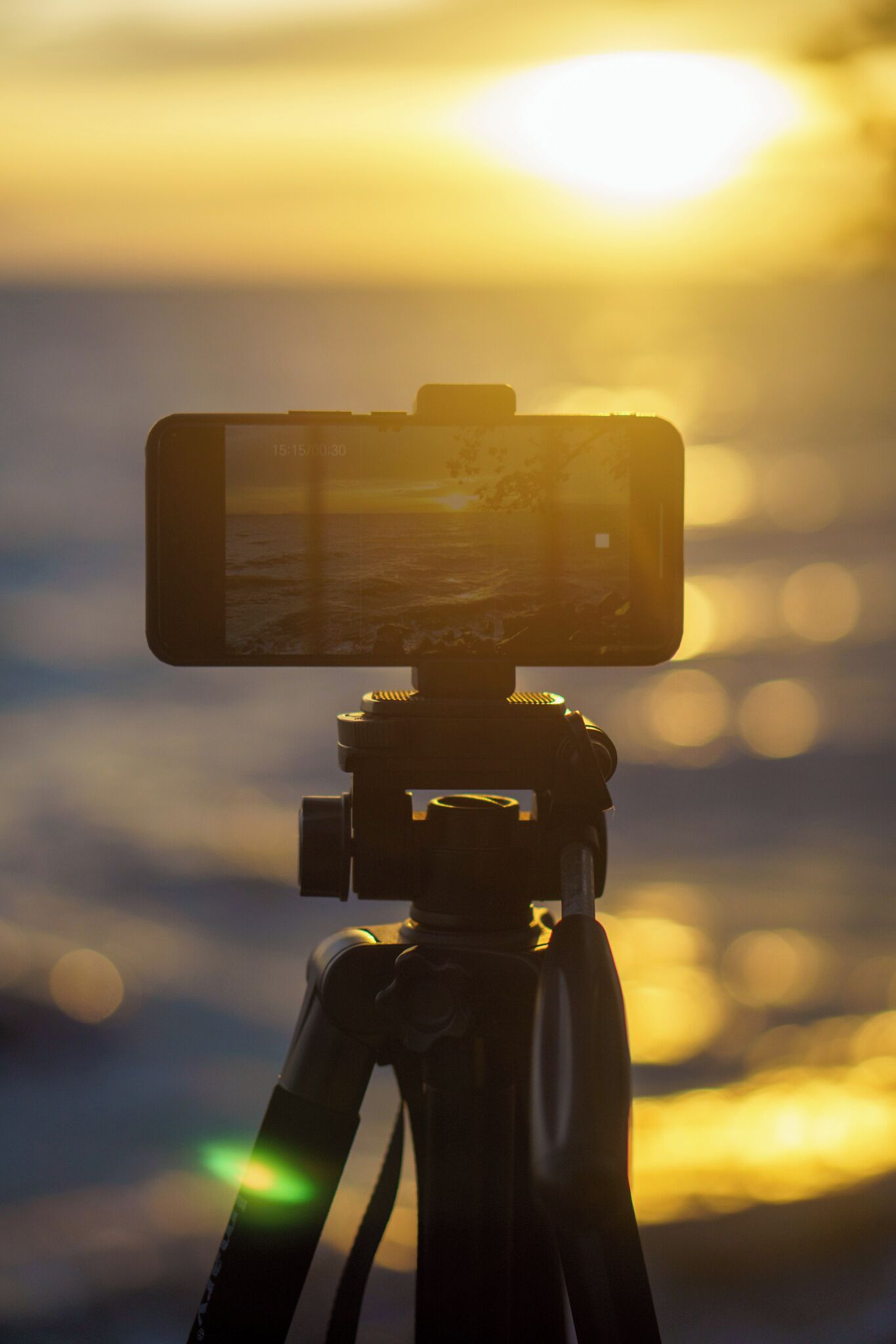 Un appareil photo fixé sur un trépied, avec un smartphone fixé à côté, le tout sur fond de coucher de soleil.