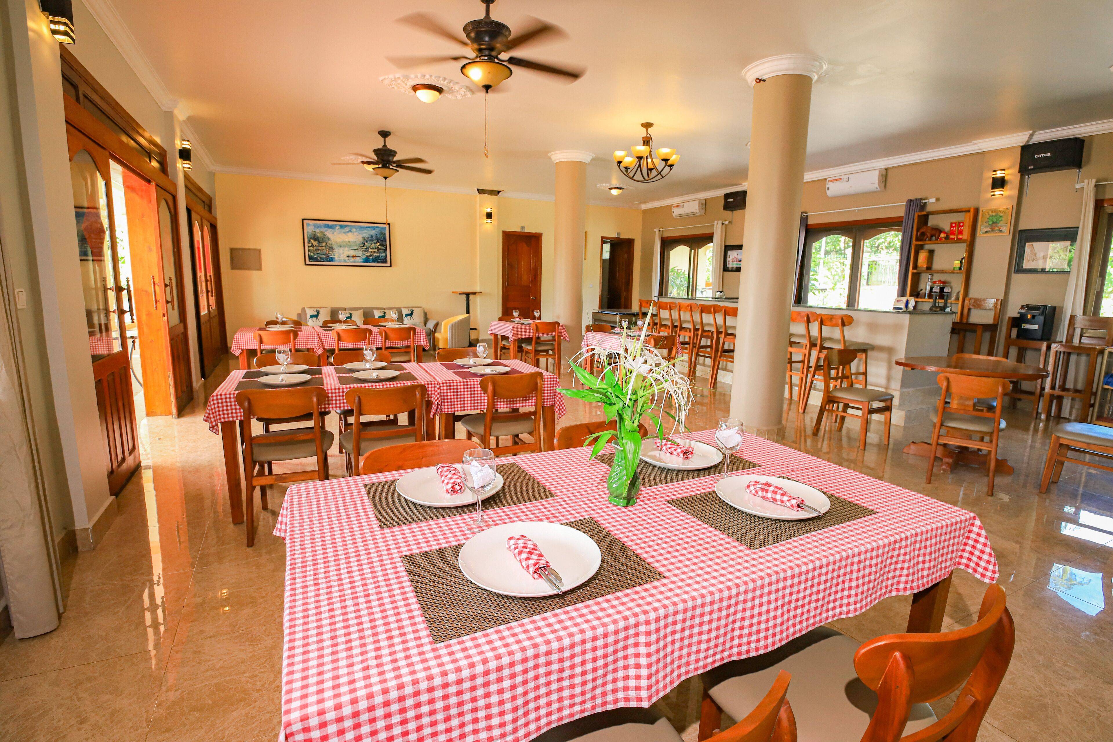 A dining area with red and white checkered tablecloths, wooden chairs, and a central vase with flowers.