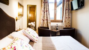 Une chambre d’hôtel avec un lit, un bureau et une chaise, une télévision et une fenêtre avec des rideaux.