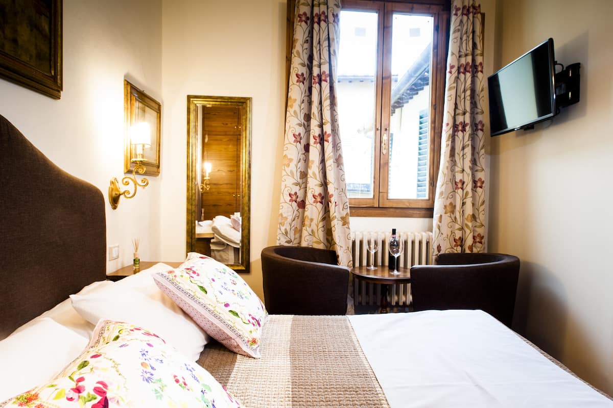 A hotel room with a bed, a desk with a chair, a television, and a window with curtains.