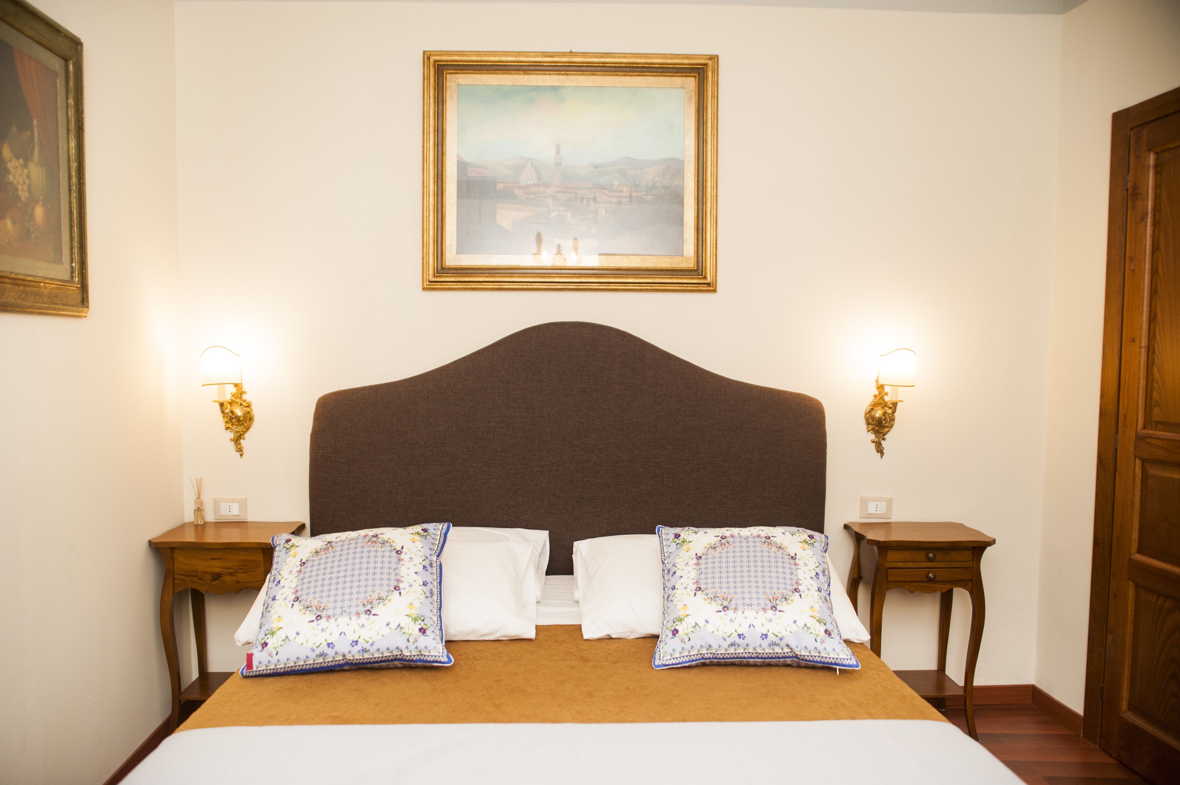 A neatly made bed with a brown headboard, two bedside tables with lamps, and a framed picture on the wall.