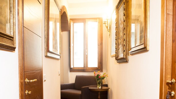 Un couloir doté d’un plancher en bois, d’un canapé, d’une petite table sur laquelle se trouve un vase, et de tableaux encadrés accrochés aux murs.