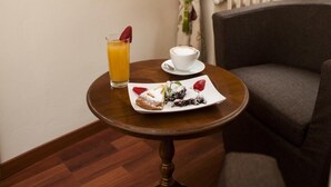 Une petite table ronde avec un verre de jus d’orange, une tasse de café et une assiette de nourriture, dans une chambre d’hôtel.