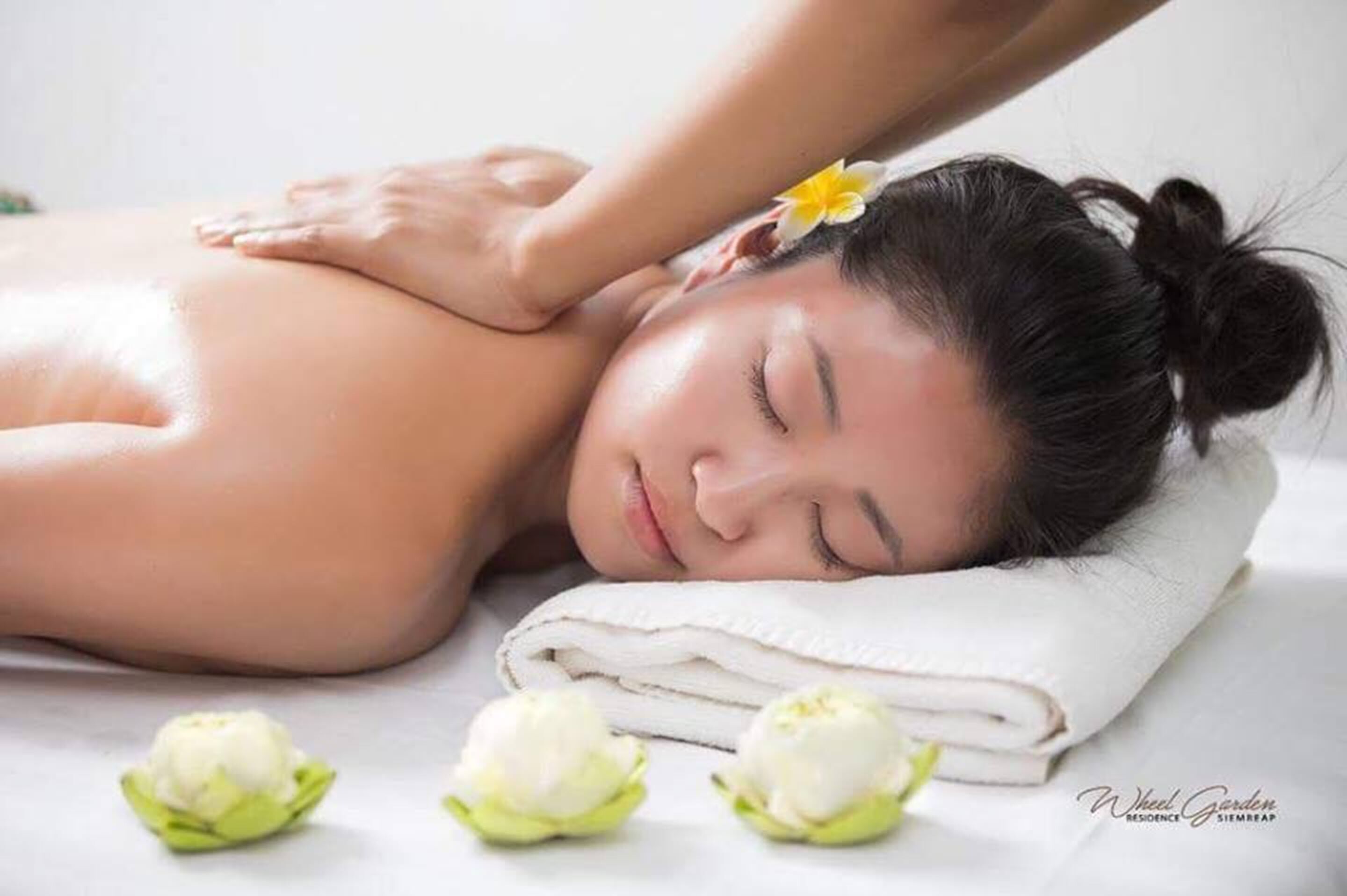 Uma pessoa recebendo uma massagem nas costas, com uma toalha e flores na cama.