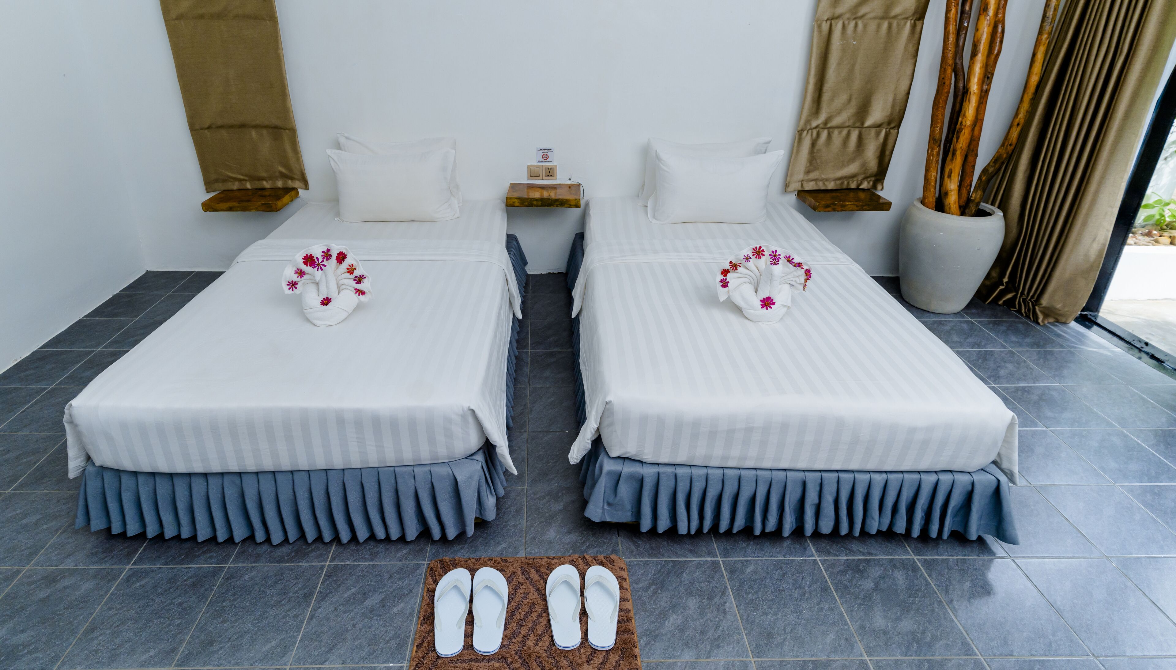 Ein Hotelzimmer mit zwei Betten, einem kleinen Tisch, einer Steckdose und einem Paar Hausschuhen auf einem Teppich.