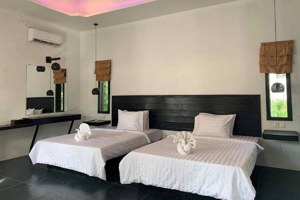 Habitación de hotel con dos camas, un espejo grande, una lámpara en el techo y una ventana con vistas.