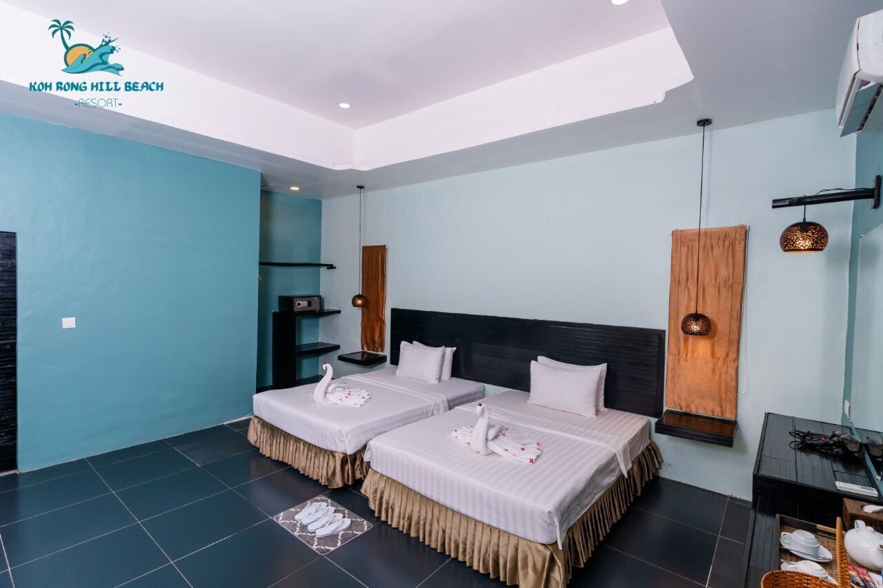 Habitación de hotel con dos camas, cabecero de madera, una mesita y un estante en la pared.