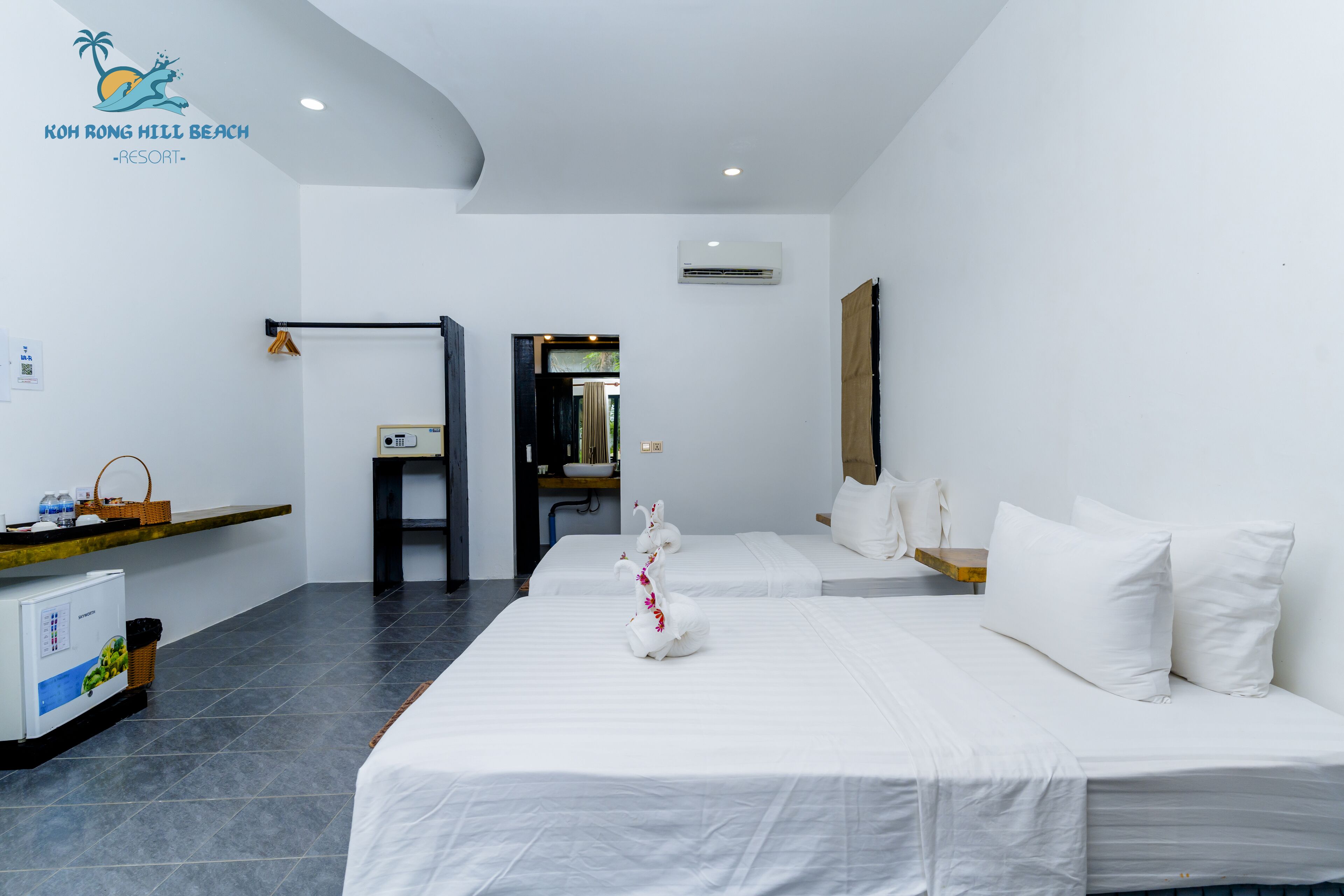 Habitación de hotel con dos camas, un escritorio pequeño, un refrigerador y aire acondicionado instalado en la pared.