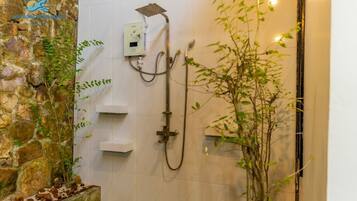 Un espacio de ducha con pared de piedra, un panel de control y una planta de bambú.