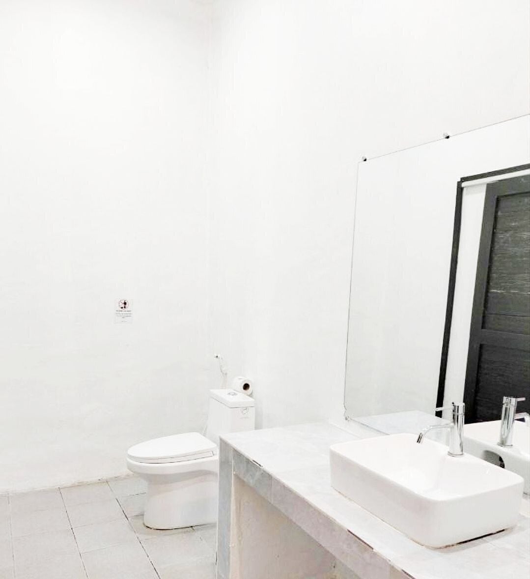 A minimalist bathroom with a white toilet, a white sink, and a large mirror.