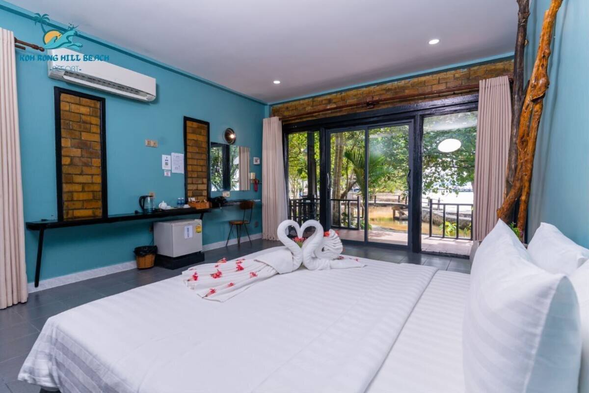 Habitación de hotel con una cama grande, un escritorio, una silla, un refrigerador pequeño y una ventana con vistas a zonas verdes.