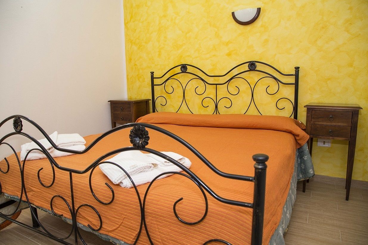 A bed with a metal frame and an orange bedspread, two wooden nightstands, and a yellow textured wall.