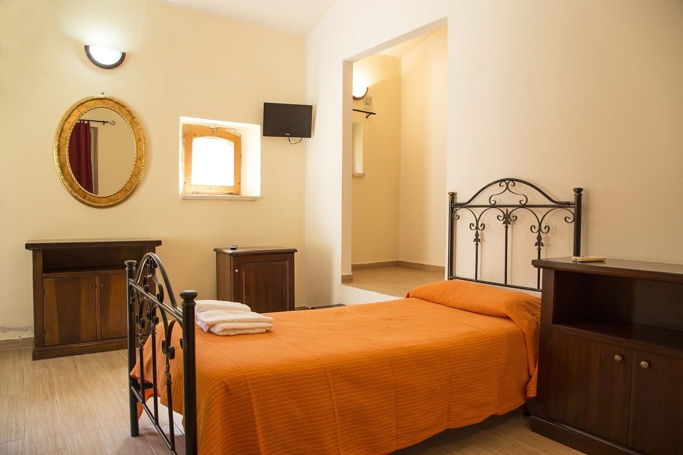 Une chambre à coucher avec un lit, une commode, un miroir, une télévision et une fenêtre.