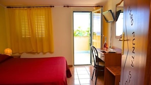 A hotel room with a bed, a desk, a chair, a television, and a sliding door to the balcony. - Villaggio Faro Punta Stilo (Guardavalle)