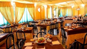 A restaurant with multiple tables, each set with plates, glasses, and cutlery. - Villaggio Faro Punta Stilo (Guardavalle)