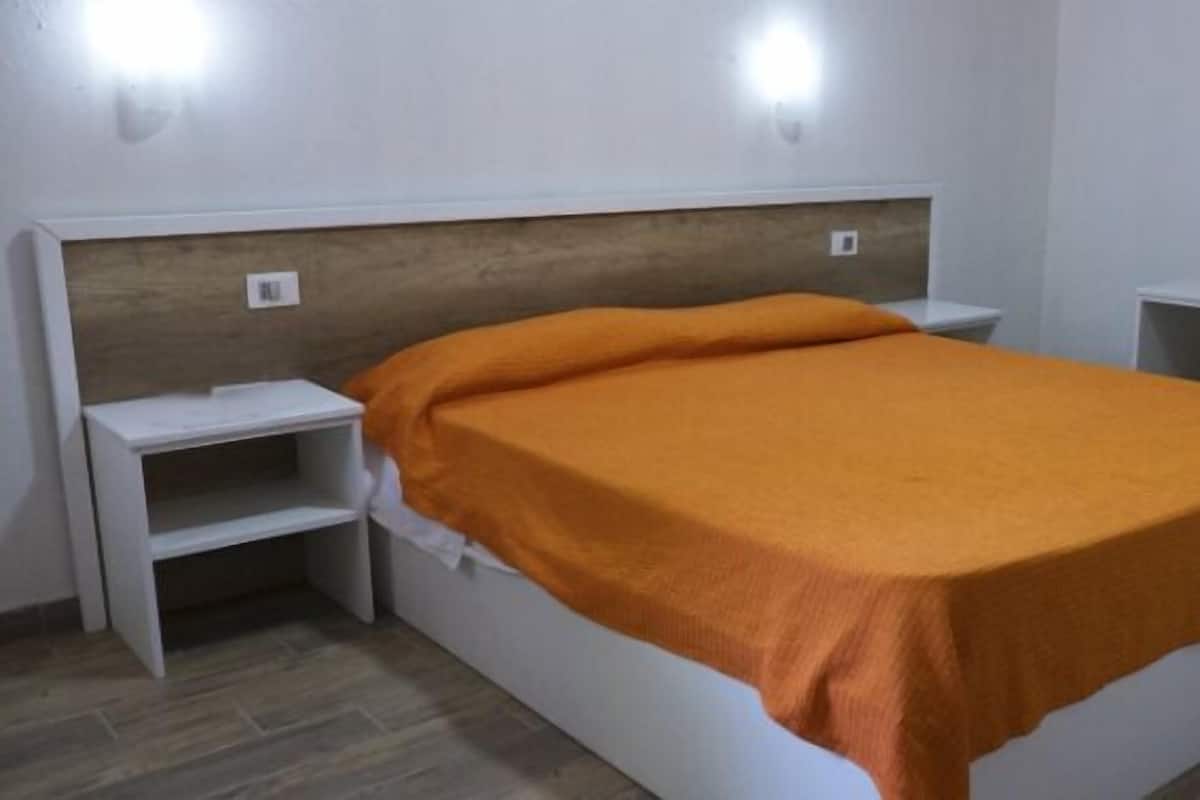 Une chambre avec un lit simple, une tête de lit en bois, des tables de chevet blanches et une armoire en bois.