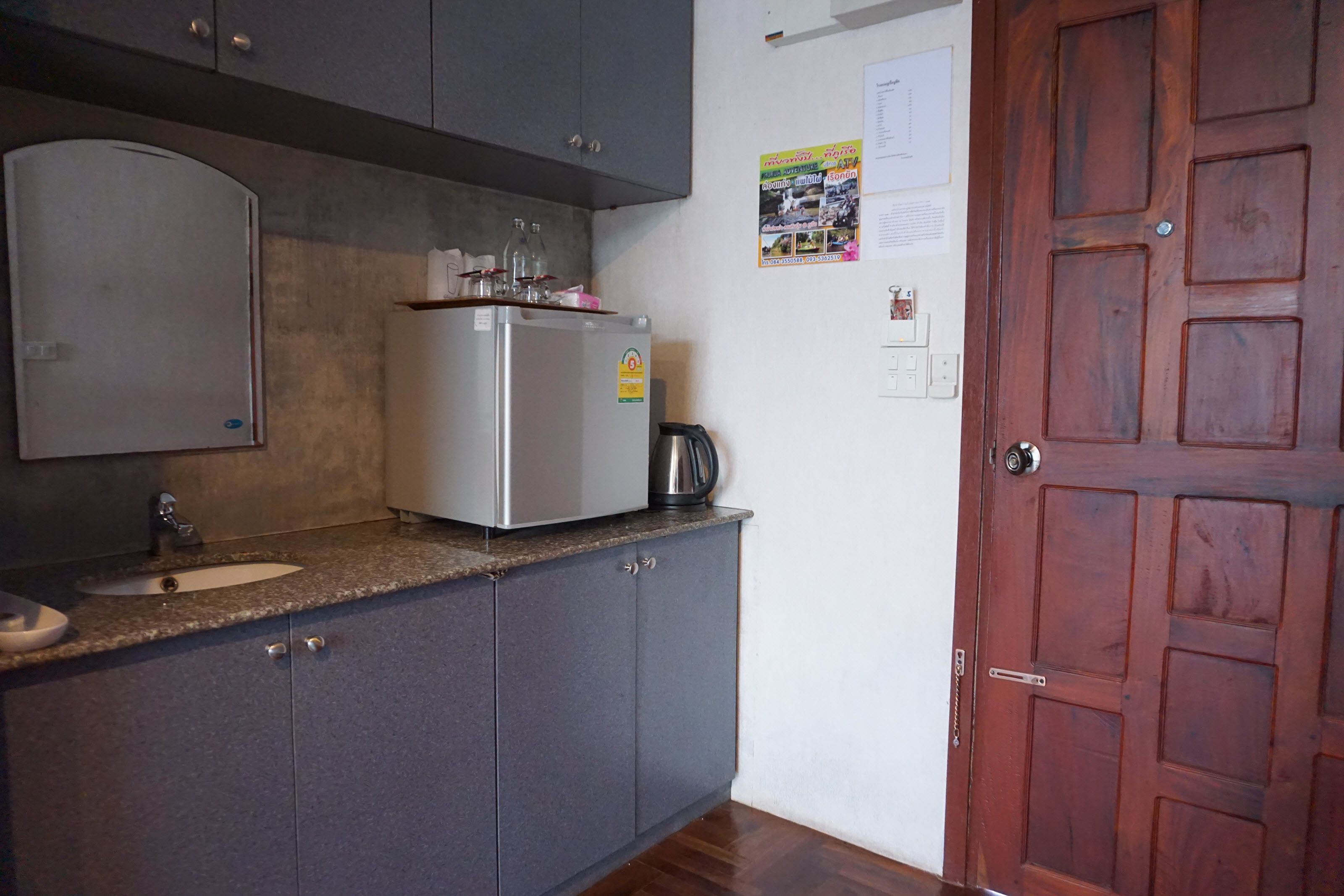 Een keuken met grijze kastjes, een roestvrijstalen koelkast, een koffiezetapparaat en een houten deur.