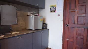 Een keuken met grijze kastjes, een roestvrijstalen koelkast, een koffiezetapparaat en een houten deur.