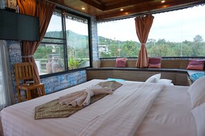 Habitación de hotel con una cama grande, una silla de madera, un televisor y vistas al exterior.