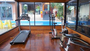 A gym with a treadmill, stationary bike, and elliptical machine. It has large windows with a view of a pool and outdoor area.