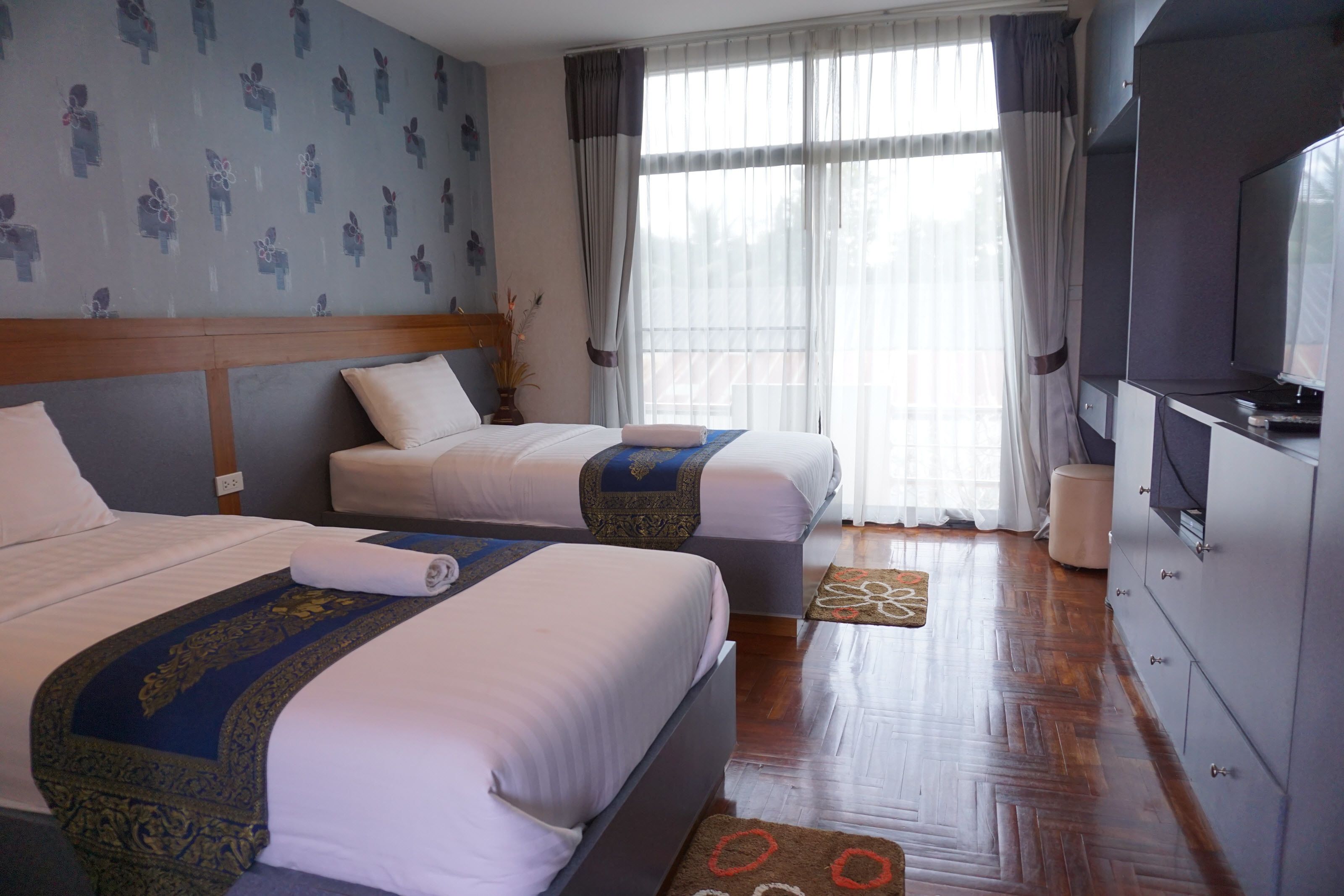Ein Hotelzimmer mit zwei Betten, einem Fernseher und einem großen Fenster mit Vorhängen.