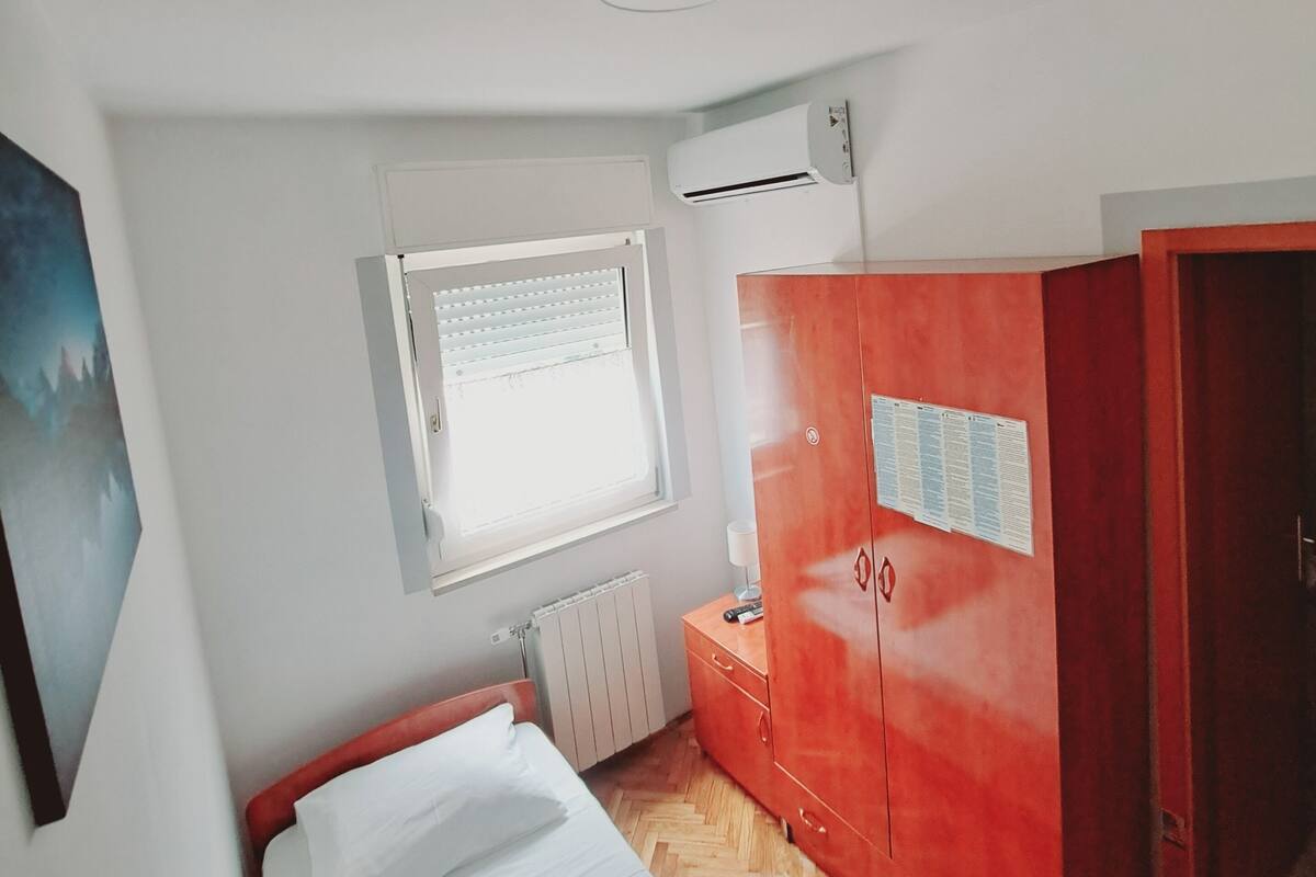 Un dormitorio con cama, armario, radiador y ventana con persianas.