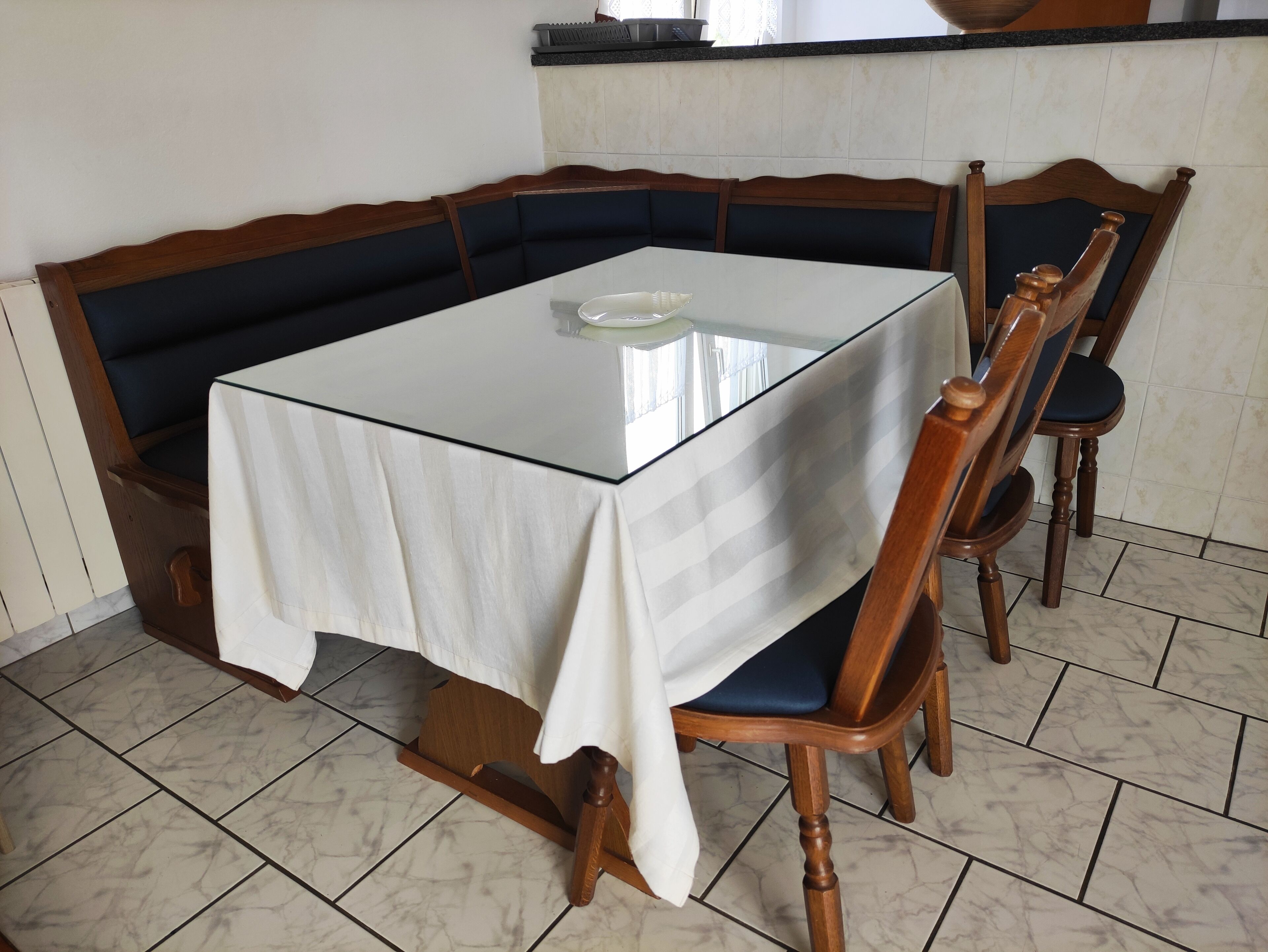 A dining area with a glass-top table, wooden chairs, and a white tablecloth.
