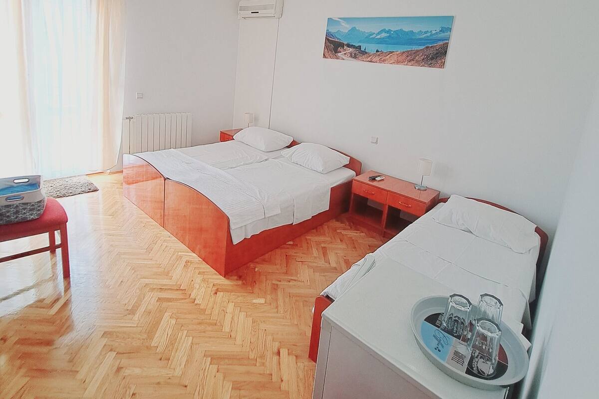 Habitación con dos camas, un escritorio con una bandeja de vasos, un radiador y un cuadro de un paisaje montañoso.