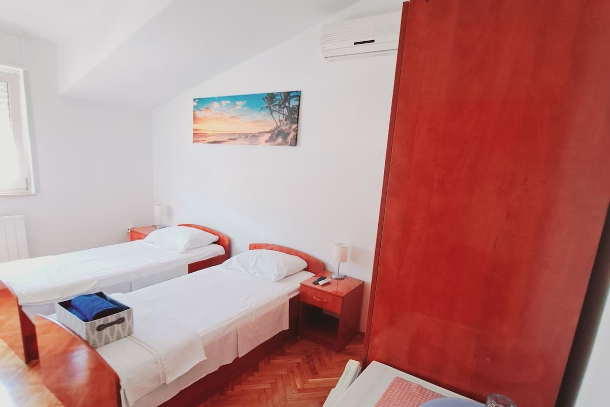 Habitación de hotel con dos camas, piso de madera, un cuadro en la pared y una pequeña mesa con un vaso.