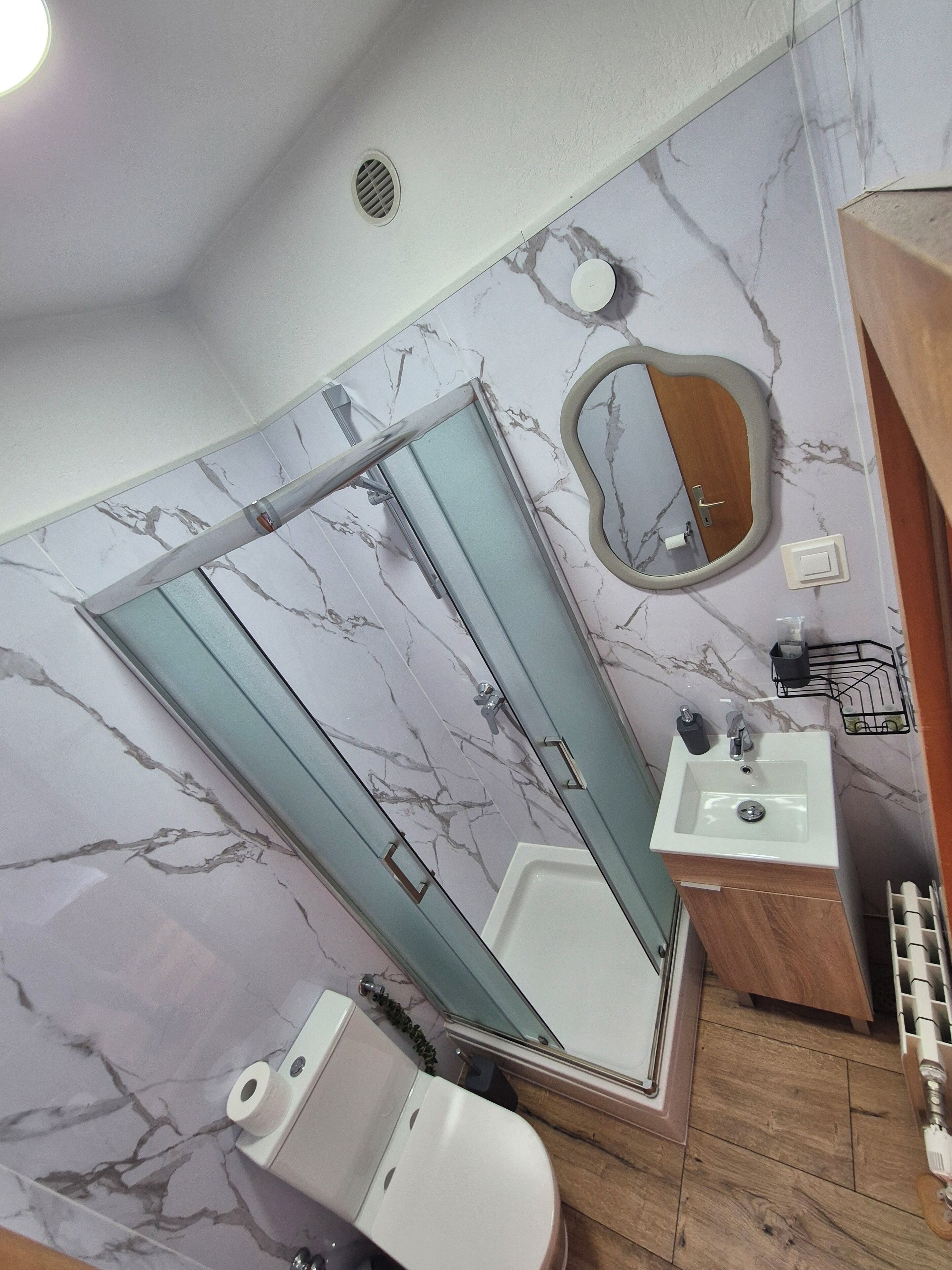A bathroom with a marble-patterned wall, a shower enclosure, a sink, and a toilet.