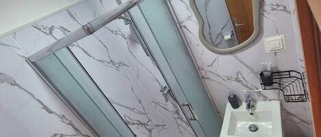 A bathroom with a marble-patterned wall, a shower enclosure, a sink, and a toilet.