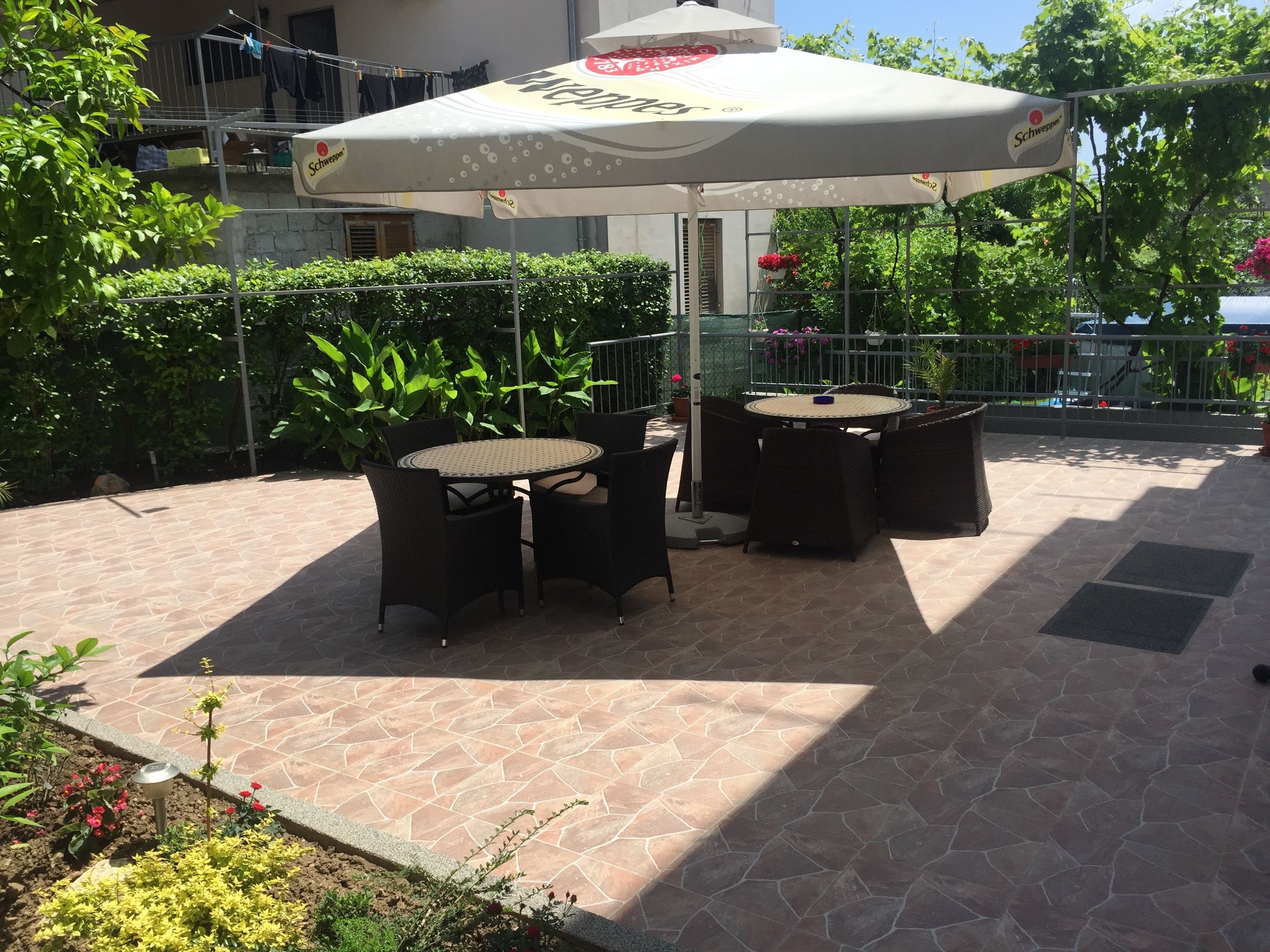 An outdoor patio with a round table and chairs, a large umbrella, and potted plants.