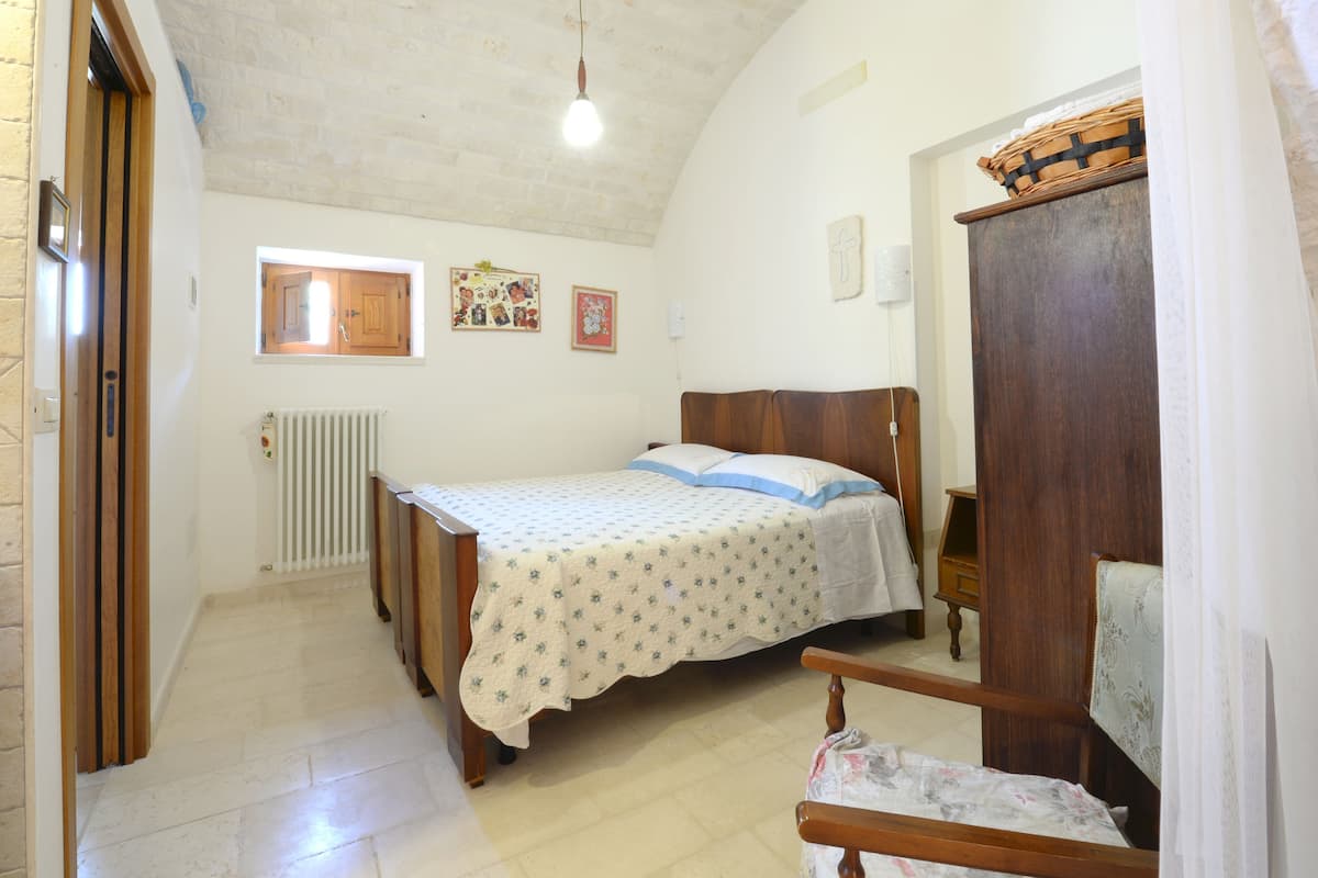 A bedroom with a bed, wooden headboard, a window, a radiator, and a wooden wardrobe.