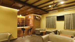 A cozy lounge area with leather sofas, a bar with wooden shelves, and a ceiling fan. - Hotel Atria (Kolhapur)