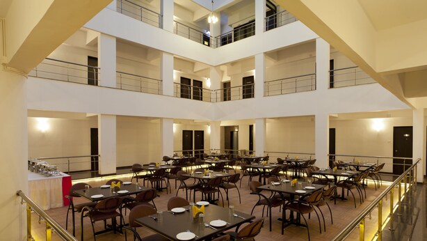 A multi-level dining area with tables and chairs, a central serving station, and a staircase connecting the floors. - Hotel Atria (Kolhapur)